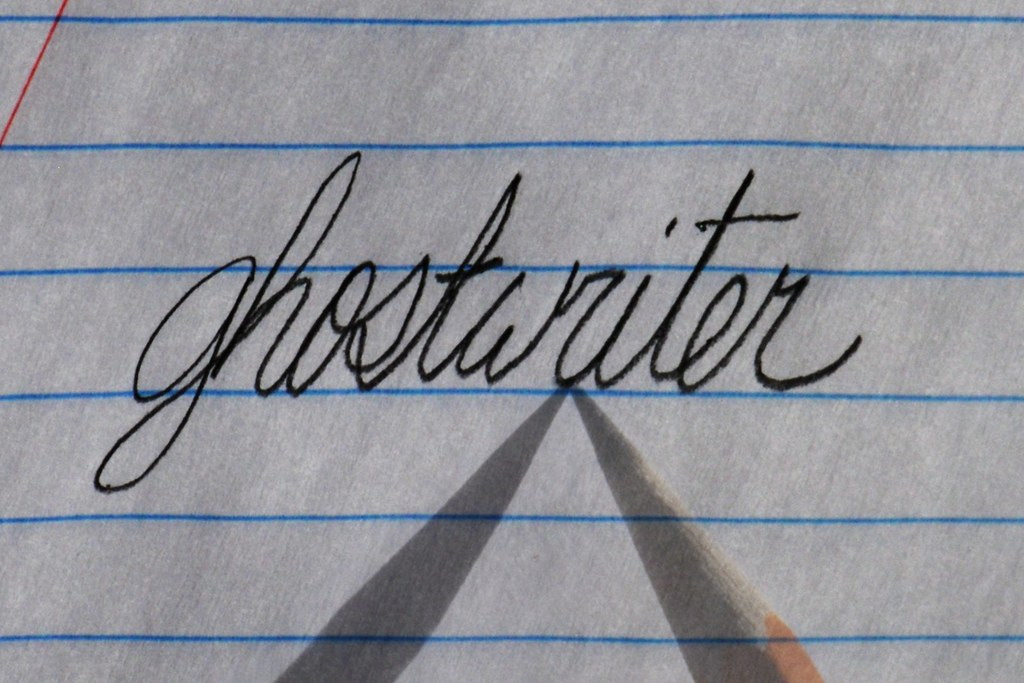 The word "ghostwriter" written in cursive on lined notebook paper. The tip of a sharpened pencil points to the word.